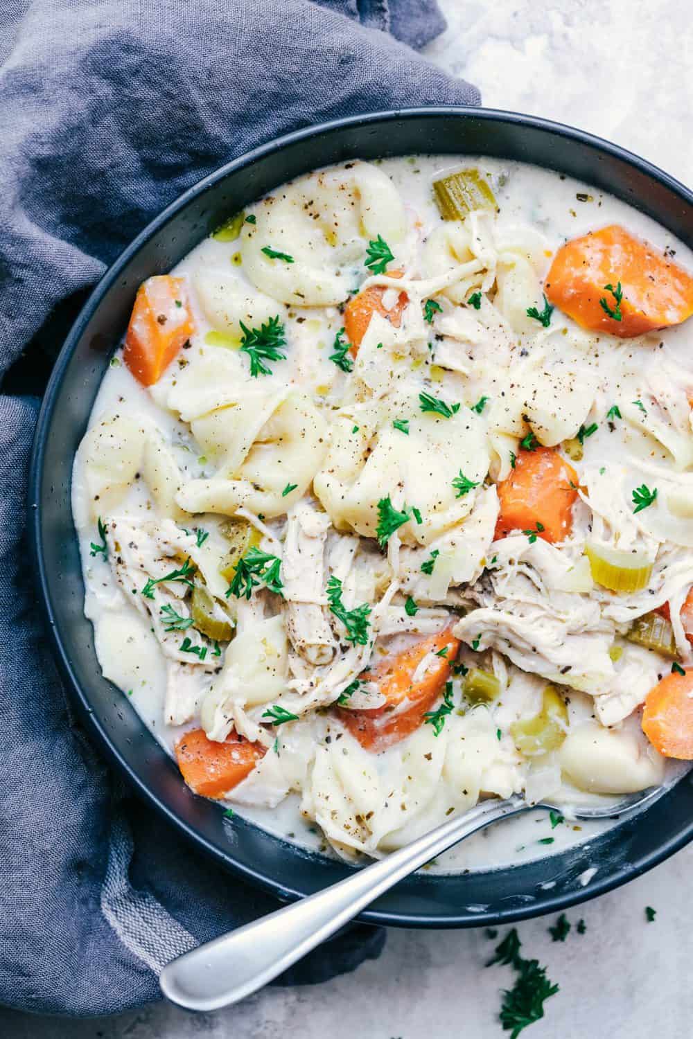 Slow Cooker Creamy Chicken Tortellini Soup is such a delicious and comforting soup. Loaded with carrots, celery, onion, chicken and tortellini, this creamy soup will become a favorite!ย Slow Cooker Creamy Chicken Tortellini Soup in a black bowl with a spoon.