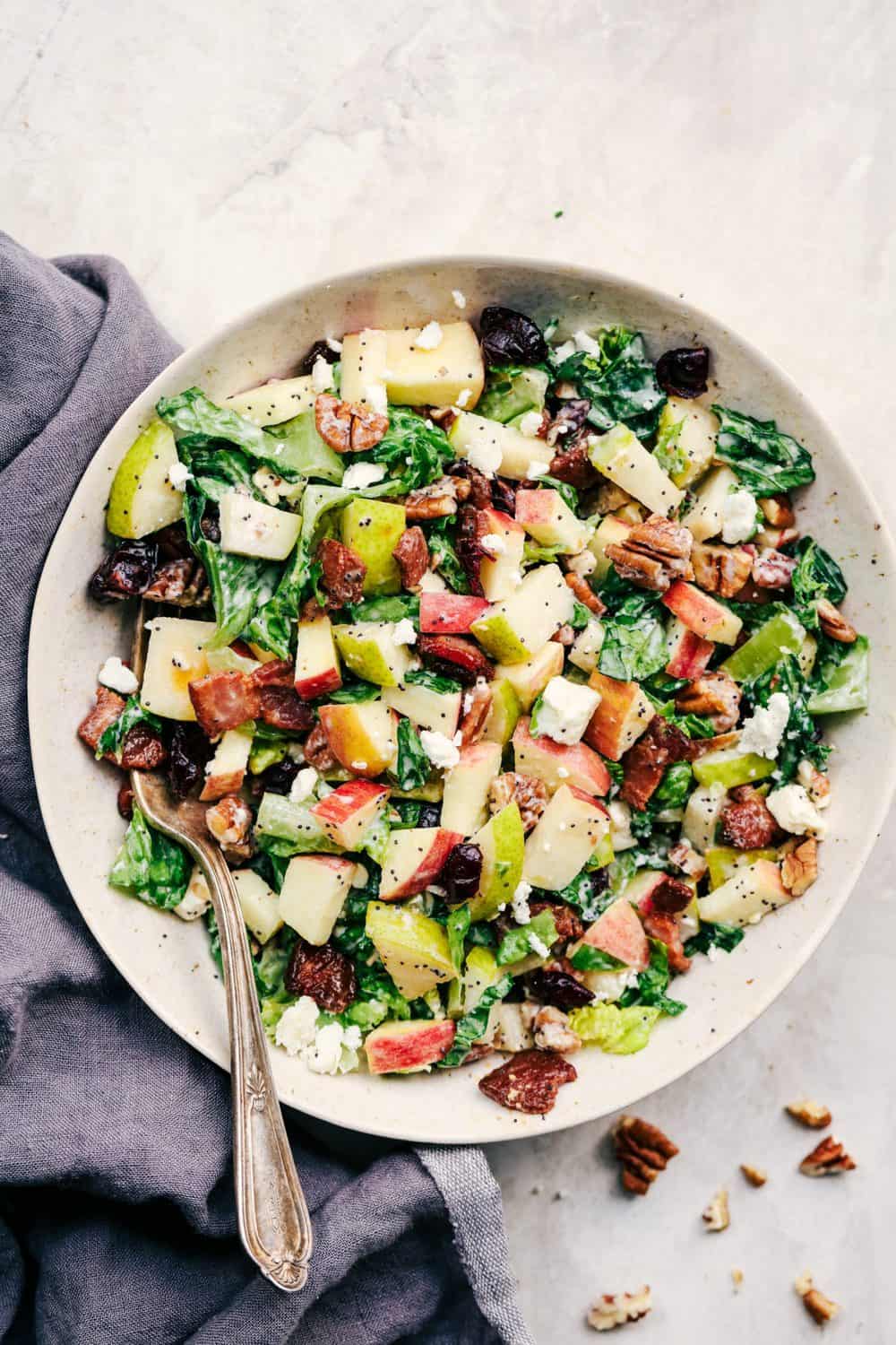 Autumn Chopped Salad with Creamy Poppyseed Dressing is all of your fall salad dreams come true! Crisp chopped apples, pears, romaine lettuce, crunchy pecans, bacon, cranberries and feta cheese combine in a creamy dressing to bring you one unforgettable salad!ย Autumn Chopped Salad with Creamy Poppyseed Dressing in a white bowl.