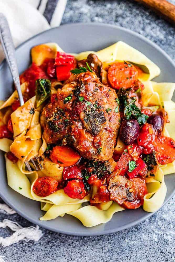 Slow Cooker Chicken Cacciatore - an easy crockpot meal loaded with tender chicken, tomatoes, bell peppers, kale, carrots and sliced mushrooms. Hearty, comforting and bursting with flavor. Slow Cooker Chicken Cacciatore over noodles on a gray plate.