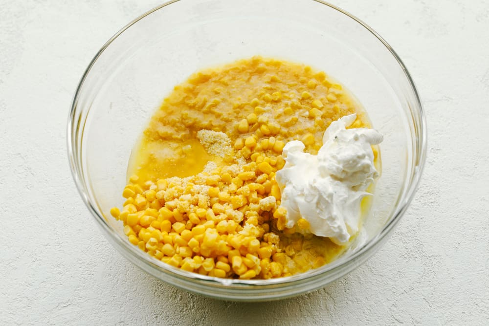 5 Ingredient Corn Casserole is in the oven in less than five minutes, it's the perfect side dish for the holidays with almost no effort at all! With an almost pudding like texture on the inside, golden crust on the outside, and buttery fluffiness throughout, this is the best quick casserole for any occasion. 5 ingredient Corn Casserole ingredients in a bowl.