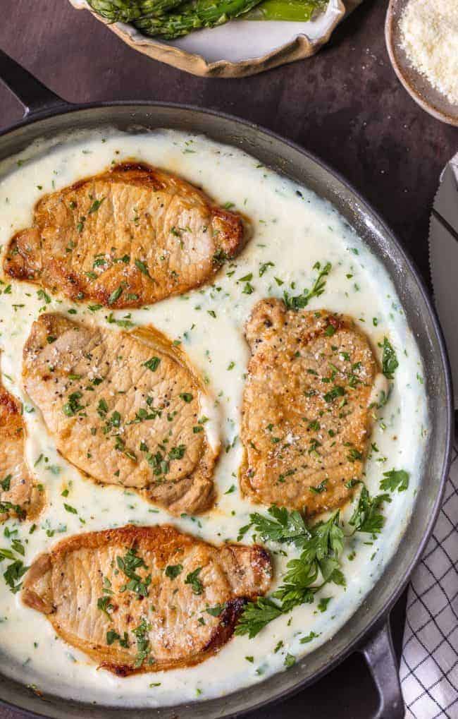 These Creamy Parmesan Pork Chops are sure to be a hit around the family table. The simple garlic parmesan sauce is oh so delicious and so easy anyone can make it in minutes.ย These Creamy Parmesan Pork Chops in a skillet.