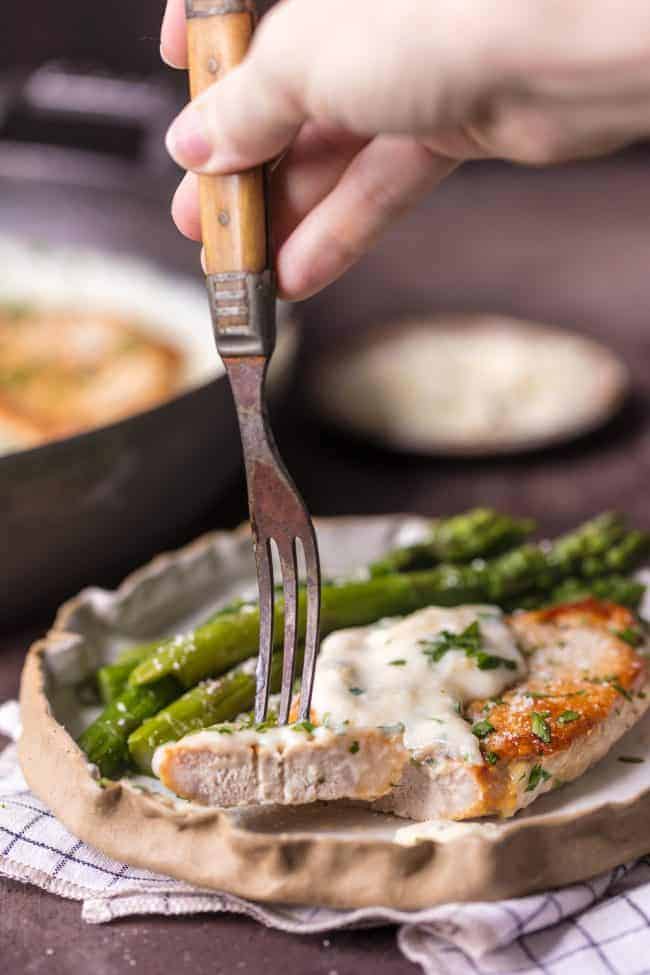 These Creamy Parmesan Pork Chops are sure to be a hit around the family table. The simple garlic parmesan sauce is oh so delicious and so easy anyone can make it in minutes.ย A bite of Creamy Parmesan Pork Chops.