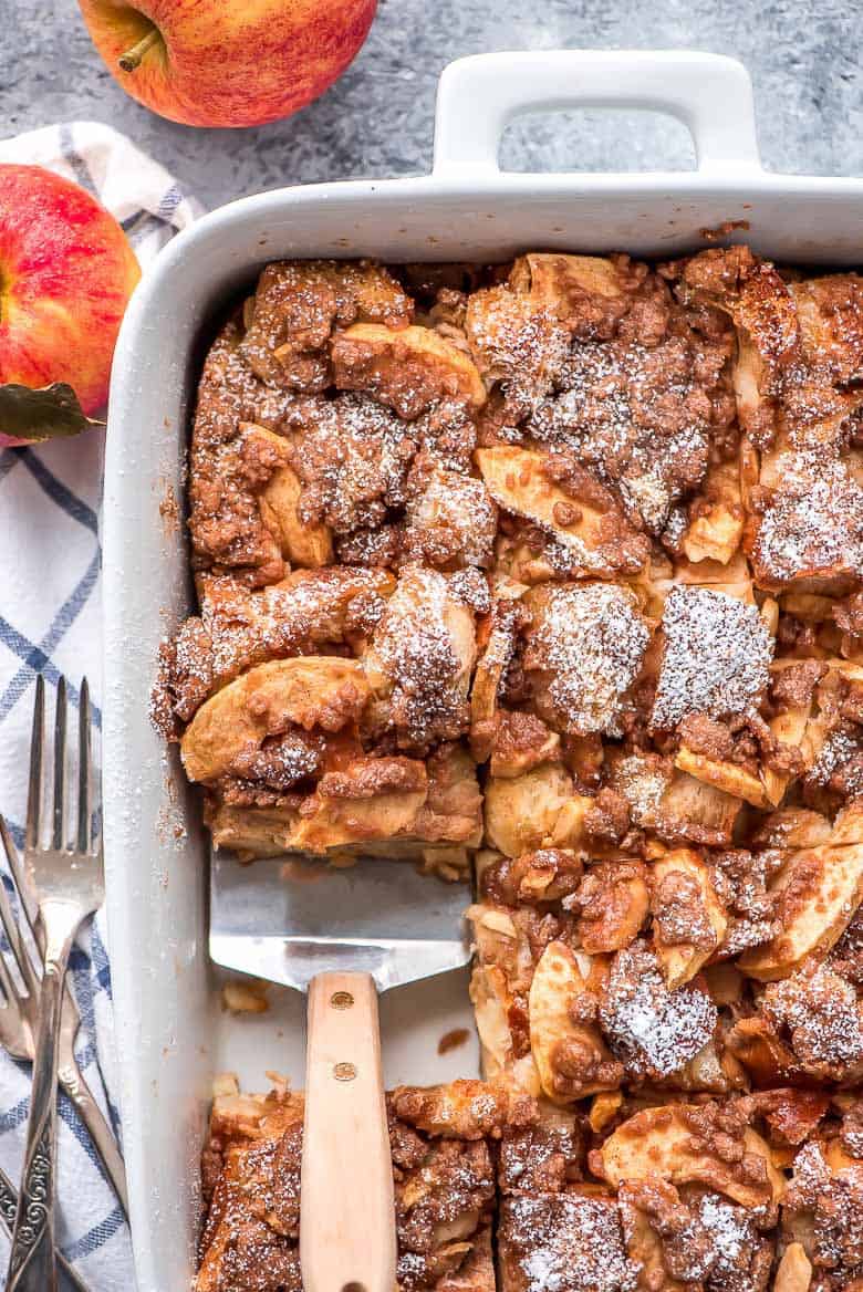 Overnight Cinnamon Apple French Toast Casserole is the perfect autumn breakfast to wake the family up to!ย Overnight Cinnamon Apple French Toast Casserole being scooped out of a white baking dish with a spatula.