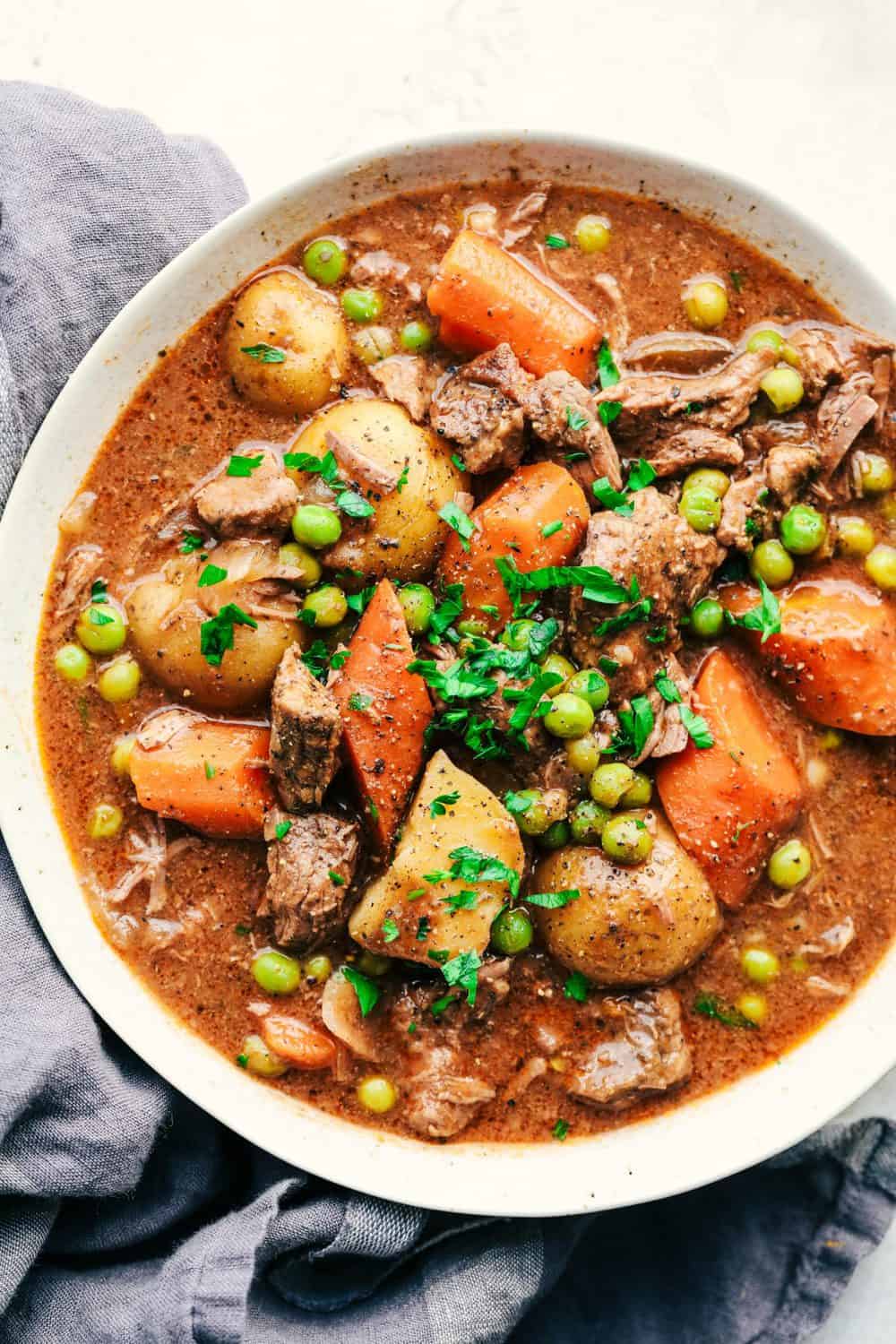 Best Ever Slow Cooker Beef Stew is the absolute perfect comforting beef stew. A thick and rich sauce filled with hearty and chunky potatoes, carrots, onions, and peas with the most amazing tender melt in your mouth beef! Best Ever Slow Cooker Beef Stew in a white bowl.