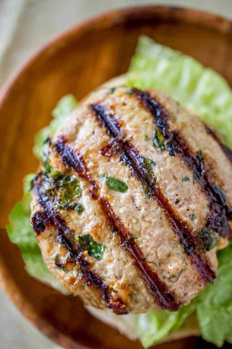 Spinach Feta Turkey Burgers with fresh spinach, salty crumbled feta cheese and a super tender turkey patty topped with lemony greek yogurt. Crazy flavorful, moist and tender Spinach Feta Turkey Burger with lettuce on a wooden plate..