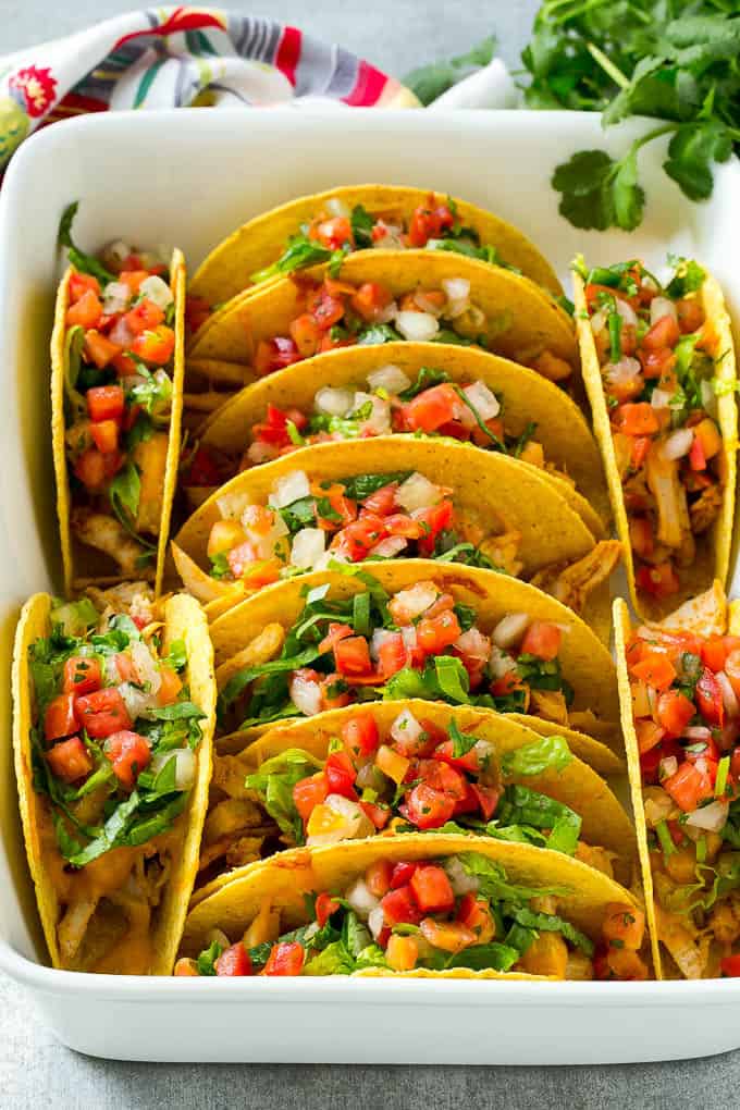 These baked chicken tacos are loaded with seasoned chicken, cheese and salsa. The perfect easy dinner for a busy day! Baked Chicken Tacos stcked in rows in a baking dish.