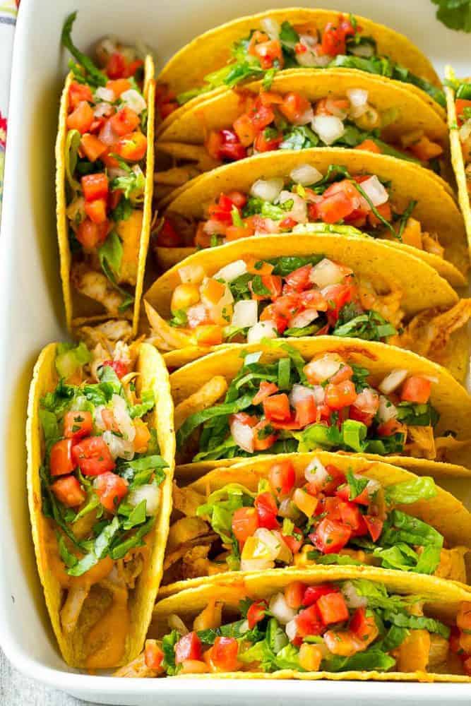 These baked chicken tacos are loaded with seasoned chicken, cheese and salsa. The perfect easy dinner for a busy day! Baked Chicken Tacos stacked in rows in a baking dish.