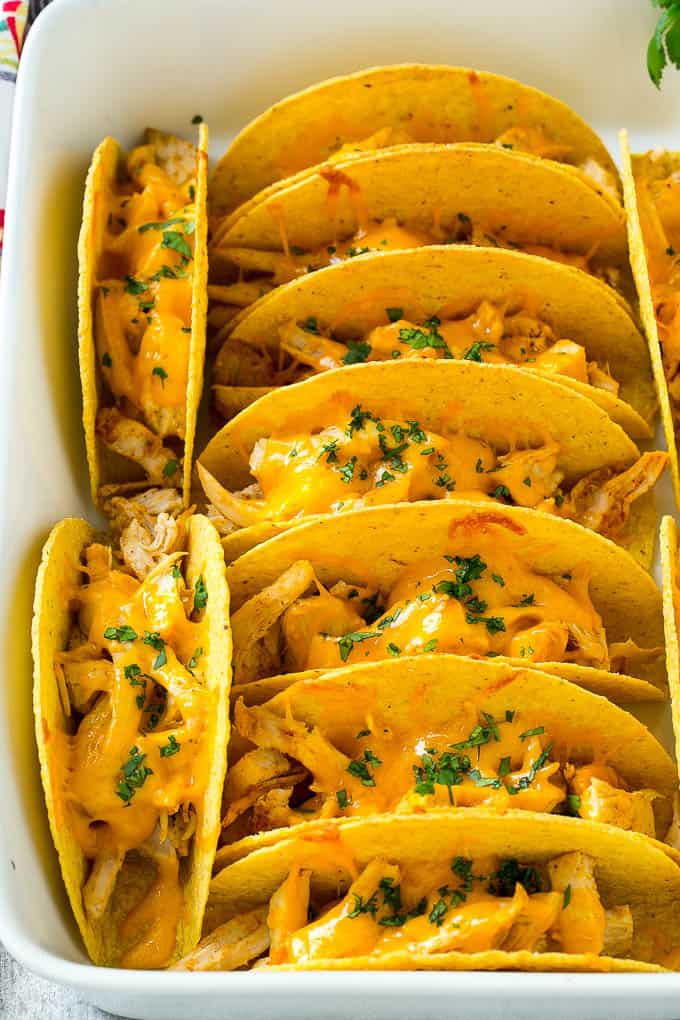 These baked chicken tacos are loaded with seasoned chicken, cheese and salsa. The perfect easy dinner for a busy day! Baked Chicken Tacos stcked in rows in a baking dish.