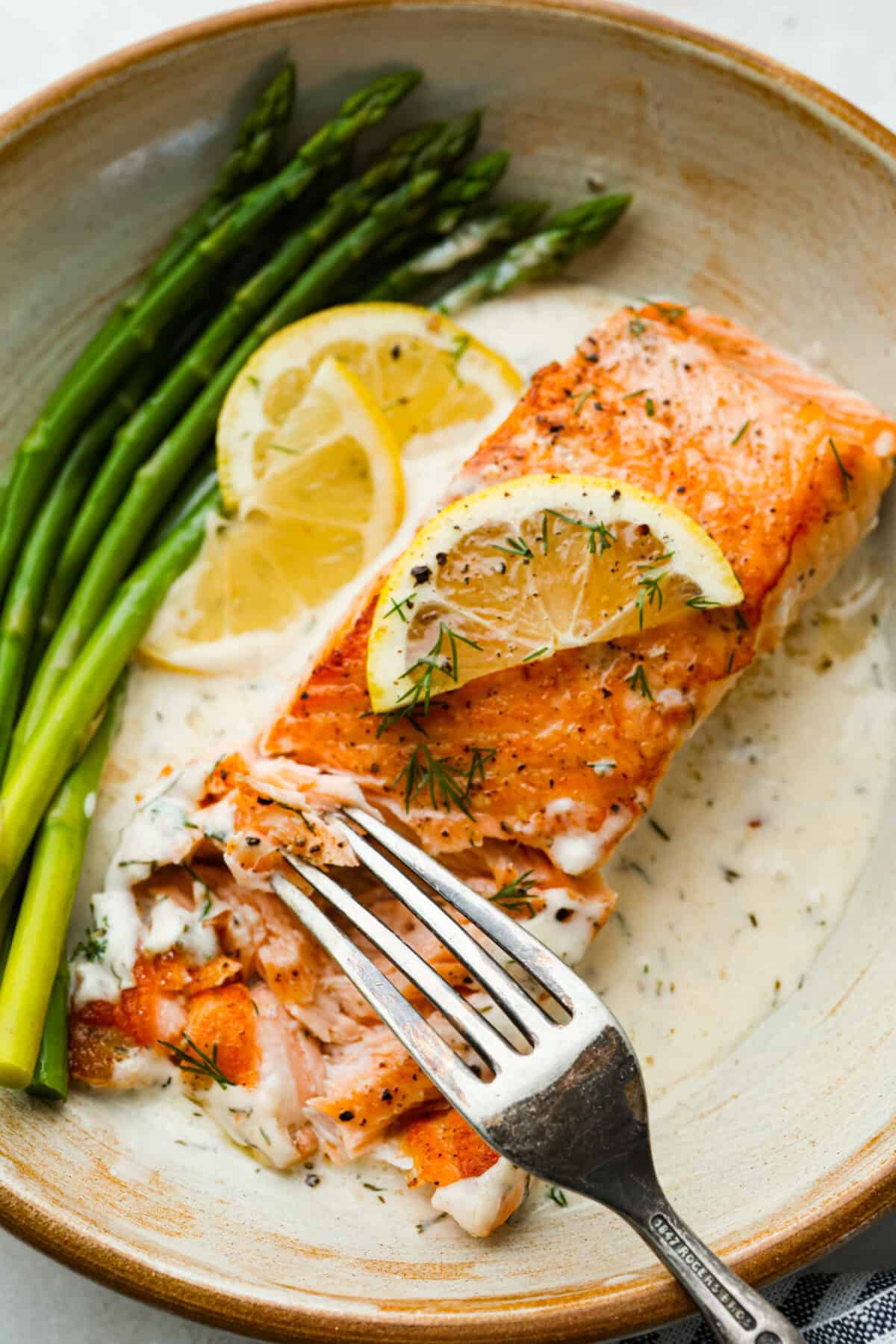 My Pan Seared Salmon has a new and improved Sauce! I added salt to bring out the flavors, and now it’s perfect! Fresh lemon juice and dill make it a match made in salmon heaven! Close up of someone cutting into a pan seared salmon filet.