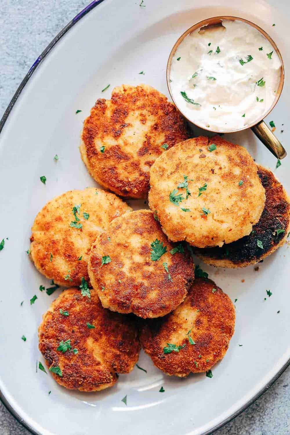 These ham mashed potato cakes are the most amazing way to use leftover mashed potatoes. They are incredibly cheesy and make for a delicious snack or appetizer! Ham mashed potato cakes on a plate with sauce on the side.