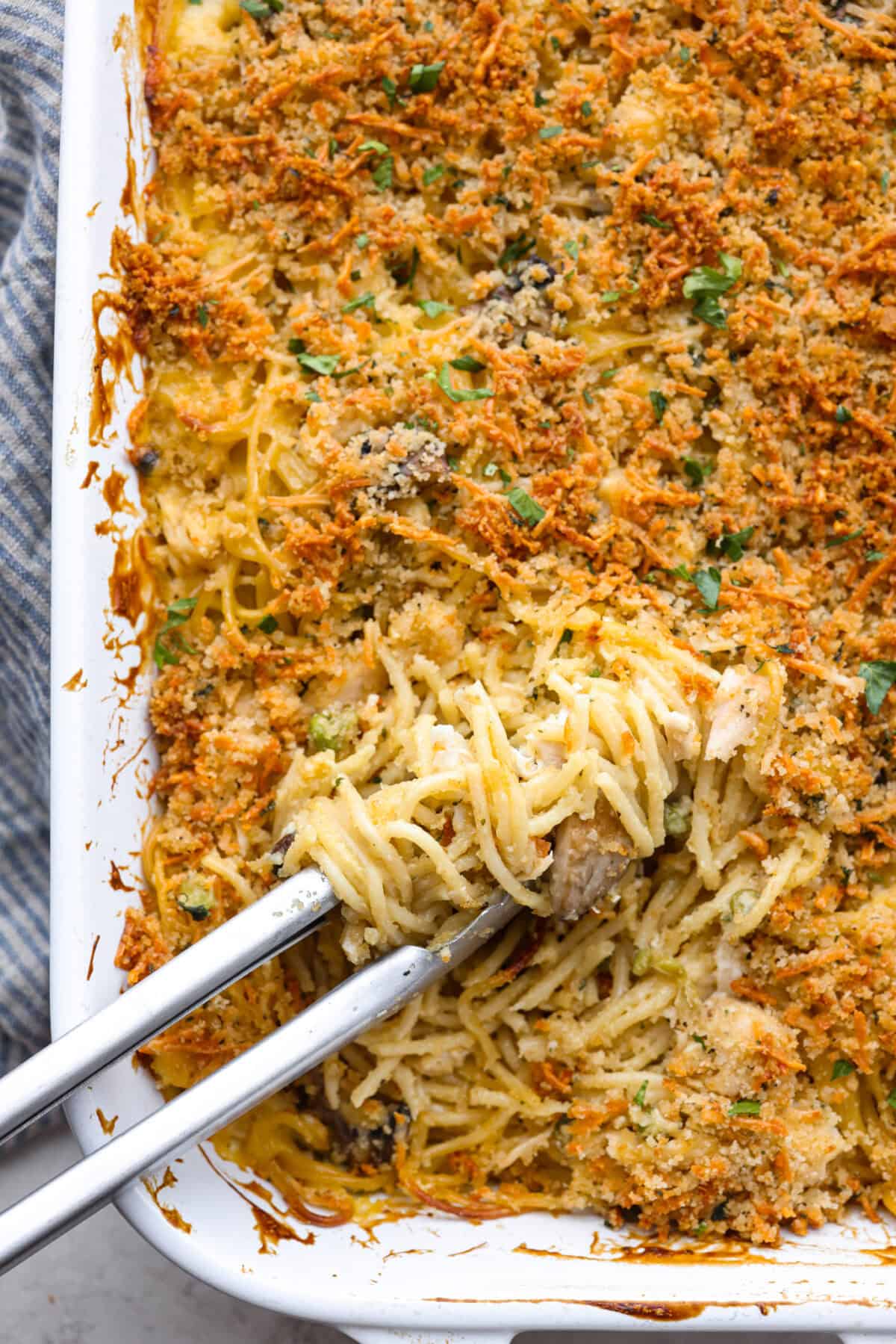 This chicken tetrazzini casserole is packed with delicious flavors and textures. It has hearty chicken, tender mushrooms, peas, and pasta, all tossed in a creamy, rich sauce. The casserole is topped with crispy, buttery breadcrumbs and a sprinkle of Parmesan cheese with the most irresistible crunch and flavor. Overhead shot of baked chicken tetrazzini casserole.