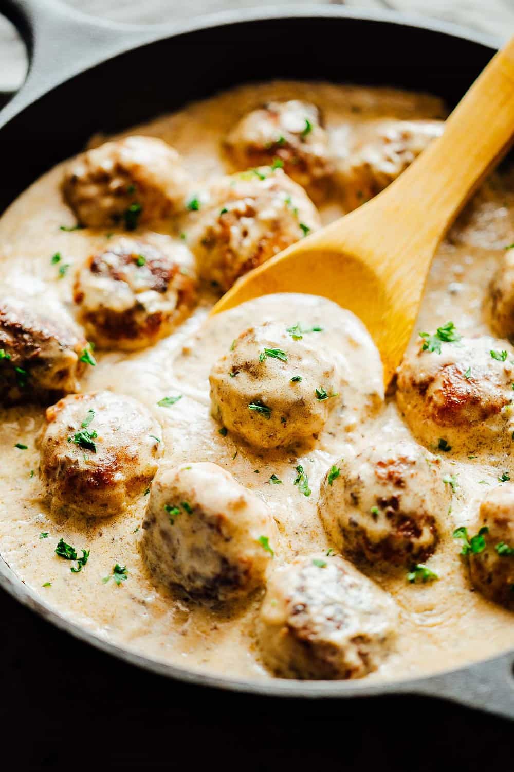 Creamy Cajun Chicken Meatballs are soft, juicy chicken meatballs slathered in a creamy gravy flavoured with cajun seasoning. This one-pot recipe is the perfect dinner option! Meatballs in sauce being stirred with a wooden spoon.