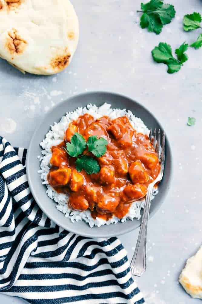This Easy Butter Chicken comes together so easily with the help of Patakโsยฎ Butter Chicken Curry Simmer Sauce and diced chicken. Serve it over rice and you have a flavorful and amazing meal for your family ready in under 30 minutes!ย Easy Butter Chicken over white rice in a grey bowl with a fork. On the side is a pita and black and white cloth.