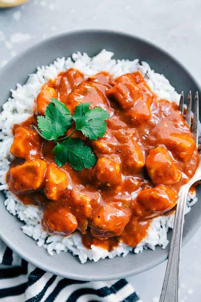 This Easy Butter Chicken comes together so easily with the help of Patakโsยฎ Butter Chicken Curry Simmer Sauce and diced chicken. Serve it over rice and you have a flavorful and amazing meal for your family ready in under 30 minutes!ย Easy Butter Chicken over white rice in a grey bowl with a fork.
