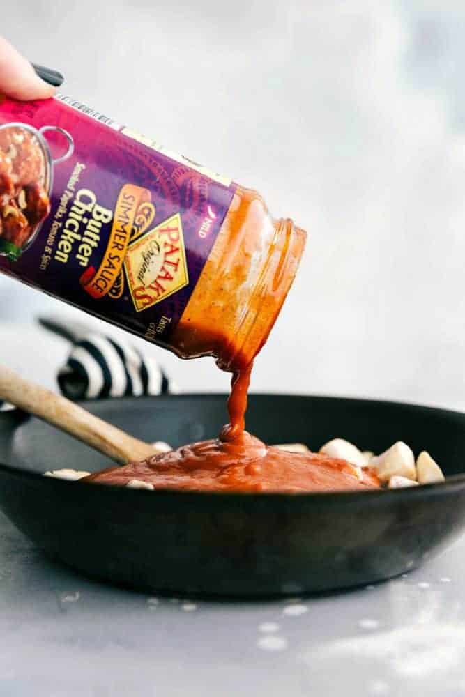 This Easy Butter Chicken comes together so easily with the help of Patakโsยฎ Butter Chicken Curry Simmer Sauce and diced chicken. Serve it over rice and you have a flavorful and amazing meal for your family ready in under 30 minutes!ย Butter chicken sauce being poured over cooked chicken in a black bowl with a wooden spoon.