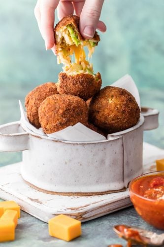 This Bacon Broccoli Cheese Arancini is a fun and unique appetizer fit for starting any delicious meal at home. Much easier than you would think and bursting with flavor. This Bacon Broccoli Cheese Arancini being pulled in half to show gooey cheese.