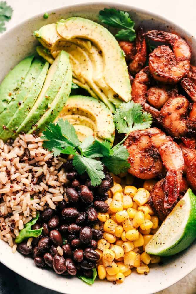 Blackened Shrimp Avocado Burrito Bowls are the perfect way to ring in the New Year with big bold flavor and a healthy meal! These are packed with blackened shrimp, brown rice, corn, black beans, and avocado. They are also great for meal prep! Blackened Shrimp Avocado Burrito Bowl with rice in a white bowl.