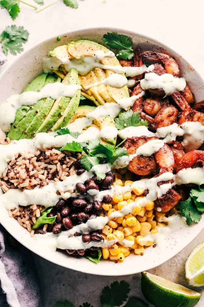 Blackened Shrimp Avocado Burrito Bowls are the perfect way to ring in the New Year with big bold flavor and a healthy meal! These are packed with blackened shrimp, brown rice, corn, black beans, and avocado. They are also great for meal prep! Blackened Shrimp Avocado Burrito in white bowl with Greek Yogurt Avocado Cilantro Ranch.