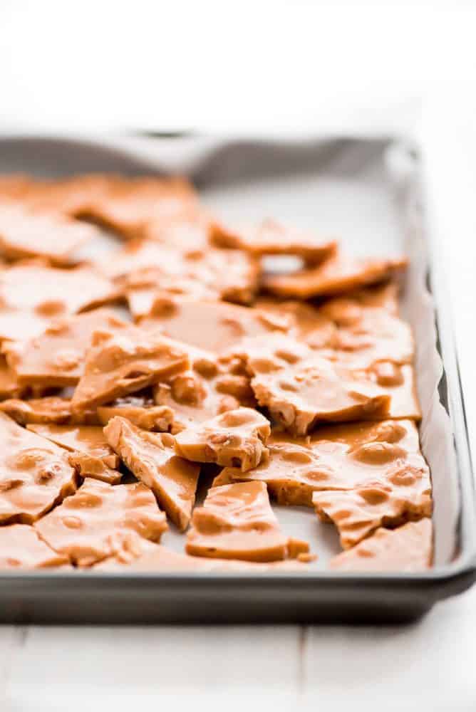 Peanut Brittle is a classic buttery and crunchy candy that no one will be able to resist munching on. It's perfect for packaging and giving away during the holidays. peanut brittle in a sheet pan laying on top of parchment paper.