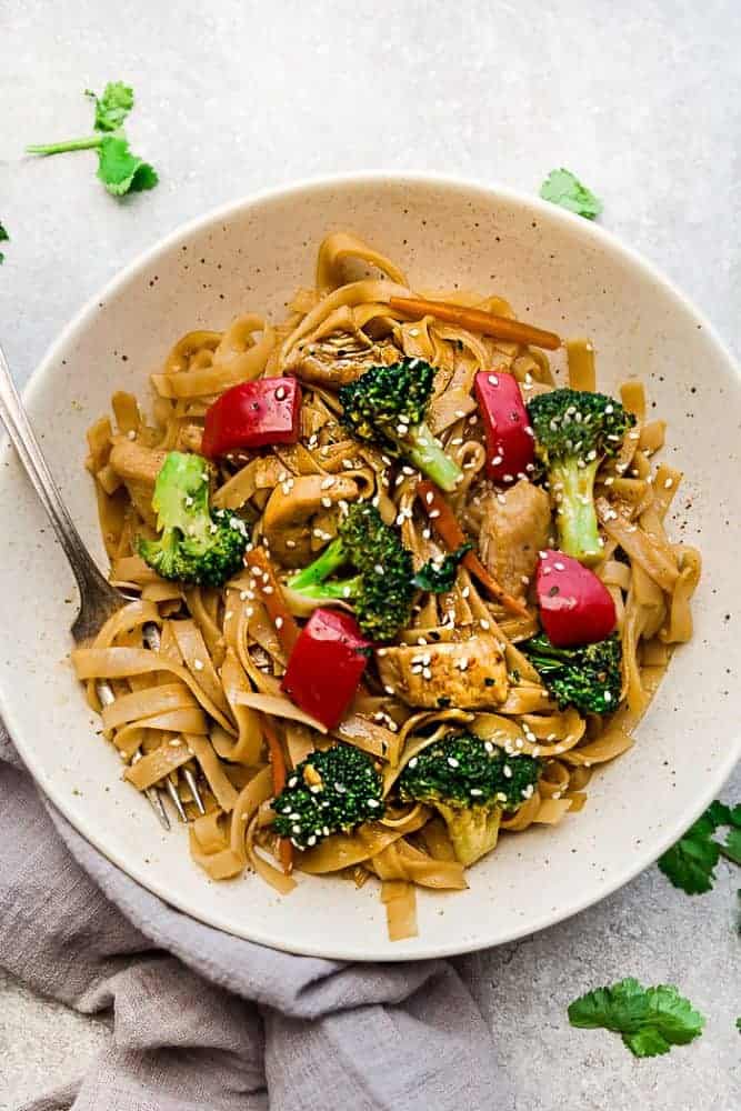 Mongolian Chicken Noodles - a one pot 30 minute meal perfect to curb those takeout cravings. Made with chicken, veggies, gluten free rice noodles and a delicious savory Asian-inspired sauce. Mongolian Chicken Noodles in a white bowl with a fork.