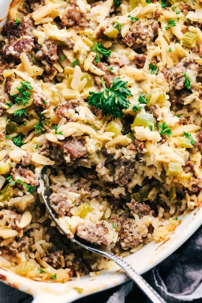 Easy Sausage and Rice Casserole is simple to make and big on flavor! Sausage, rice, celery, and onions all bake in a creamy sauce and the result will wow the entire family!ย Easy Sausage and Rice Casserole in a white dish with a metal spoon.