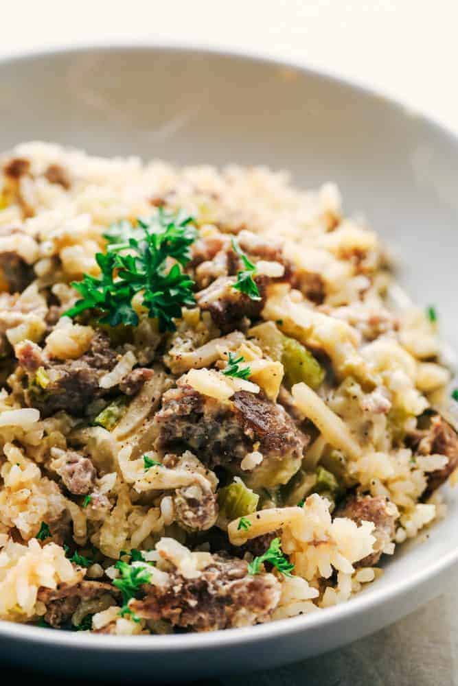 Easy Sausage and Rice Casserole is simple to make and big on flavor! Sausage, rice, celery, and onions all bake in a creamy sauce and the result will wow the entire family!ย Easy Sausage and Rice Casserole in a white bowl with garnish on top.