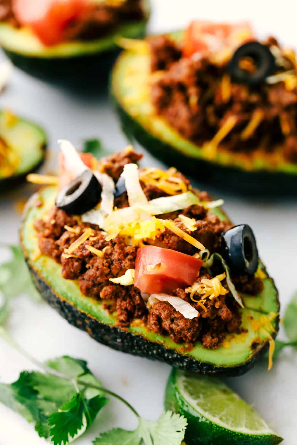 Taco stuffed avocadosย are a healthy twist on tacos and you will love the textures of this flavorful version. Ripe avocados stuffed with seasoned beef and loaded with all your favorite taco toppings! Side view of a taco stuffed avocado. The avocado is garnished with tomatoes, olives, cheese, cilantro, and a lime wedge.