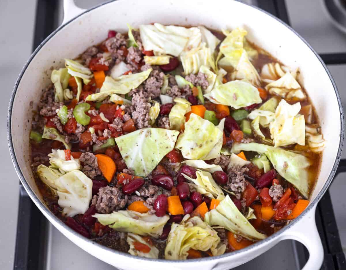Beef and Cabbage soup is filled with seasoned ground beef, cabbage, carrots, celery, kidney beans, and diced tomatoes. It is hearty, delicious, and full of flavor! This is a great soup to serve on a cold day or to help you get in the spirit of St. Patrick's Day while keeping your nutrition goals in check. Overhead shot of all of the ingredients mixed together in a pot.