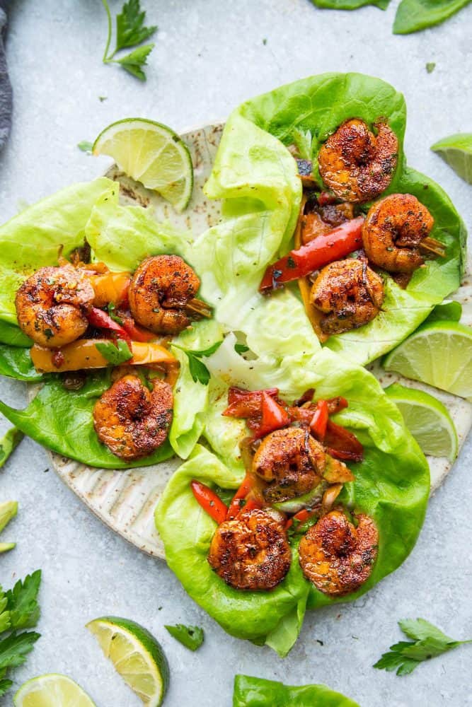 These Cilantro Lime Shrimp Lettuce Wraps are fresh, flavorful and super easy to make! They make the perfect handheld appetizers or a light and healthy low-carb lunch or dinner! Cilantro Lime Shrimp Lettuce Wraps on a tan plate with sliced lime on the side.