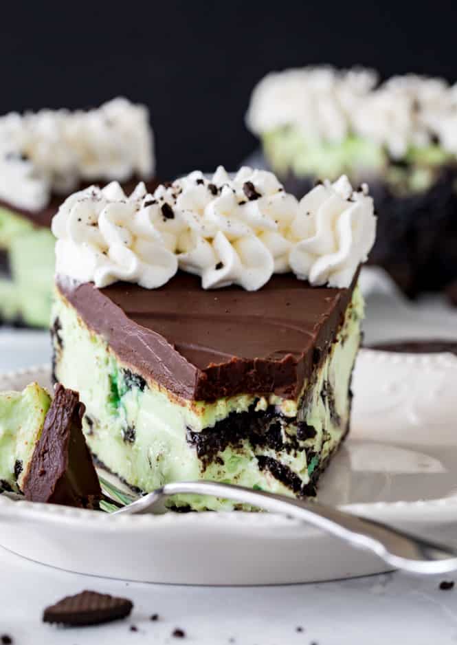 A creamy Mint Oreo Cheesecake served on a crisp Oreo cookie crust and made with no waterbath required! Top it off with a dark chocolate ganache and whipped cream for a decadent mint and chocolate treat! A closeup of Mint Oreo Cheesecake on a white plate with a metal fork.