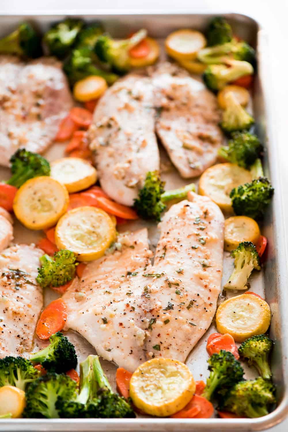 Baked Tilapia and Roasted Veggies is a low calorie and high protein dish that comes together in less than 25 minutes! Light and tasty in every bite!ย Baked Tilapia and Roasted Veggies on a pan
