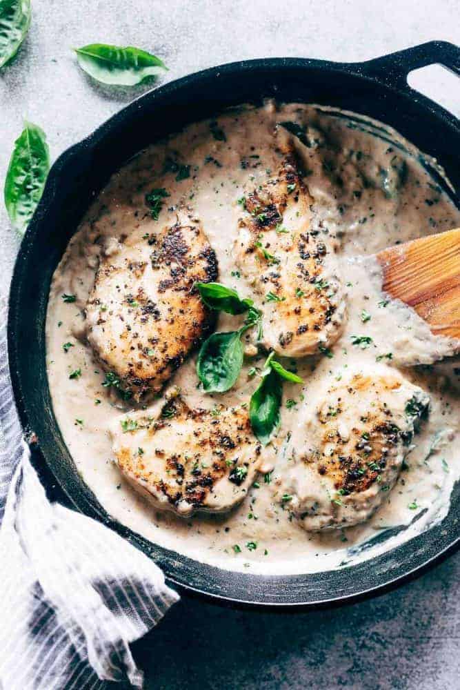 Fast and easy creamy herb chicken takes only 30 minutes to make. This is a delicious recipe that's low on the calories and is creamy but without the heavy cream! Easy creamy herb chicken in a pan with a spatula garnished with parsley and basil