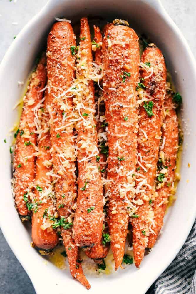 Garlic Butter Parmesan Carrots are roasted to absolute tender perfection in the most amazing garlic butter parmesan coating! These are the best carrots I have ever had!ย Garlic Butter Parmesan Carrots in a white dish.