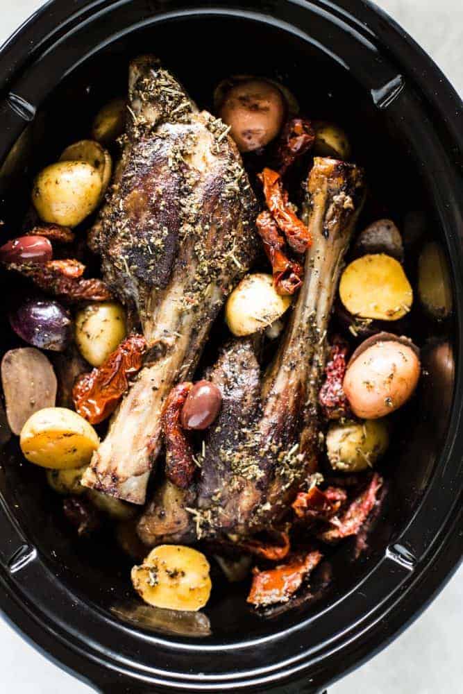 Slow Cooker Greek Lamb Shanks are fall off the bone tender and rubbed in the best greek spices. Potatoes, sun-dried tomatoes, and kalamata olives all cook to perfection in the slow cooker and make such a delicious meal in one!ย Slow Cooker Greek Lamb Shanks in a slow cooker.