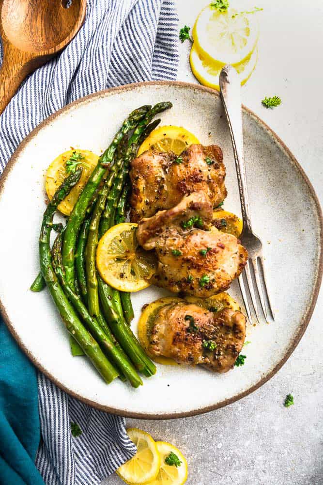 Instant Pot Lemon Garlic Chicken is simple and easy to make in the pressure cooker and perfect for busy weeknights. The chicken cooks up tender and juicy in a buttery lemon garlic sauce. Instant pot lemon garlic chicken on a plate with asparagus and lemon slices.