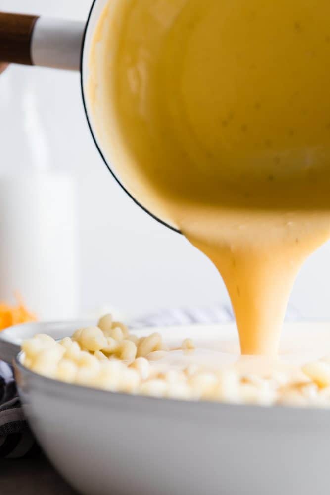 This Baked Macaroni and Cheese comes together quick and easy. Homemade cheese sauce generously covers noodles and is baked to a rich, bubbly, golden brown perfection. When served with a hearty side of veggies, this indulgent dish becomes the perfect weeknight meal. Cheese being poured over macaroni.
