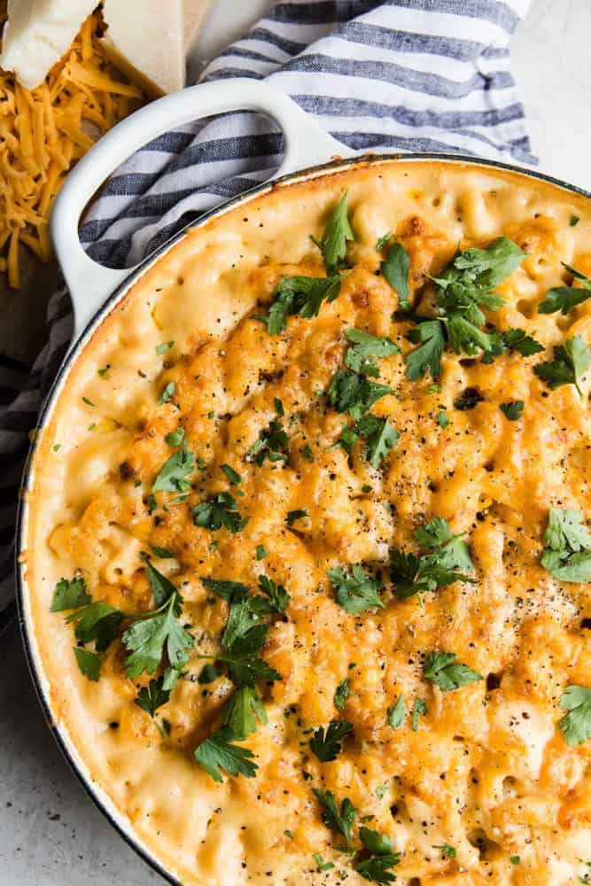 This Baked Macaroni and Cheese comes together quick and easy. Homemade cheese sauce generously covers noodles and is baked to a rich, bubbly, golden brown perfection. When served with a hearty side of veggies, this indulgent dish becomes the perfect weeknight meal. Baked Macaroni and Cheese in a white pot with a grey and white cloth.