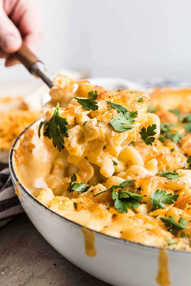 This Baked Macaroni and Cheese comes together quick and easy. Homemade cheese sauce generously covers noodles and is baked to a rich, bubbly, golden brown perfection. When served with a hearty side of veggies, this indulgent dish becomes the perfect weeknight meal. Baked Macaroni and Cheese being spooned out of a white pot.