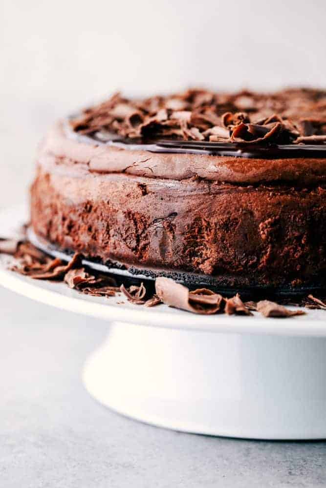 Death by chocolate cheesecake has an Oreo crust with creamy, decadent, and rich chocolate cheesecake. Topped with chocolate ganache, this is a chocolate lover's dream come true! Death by Chocolate Cheesecake on a cake stand.