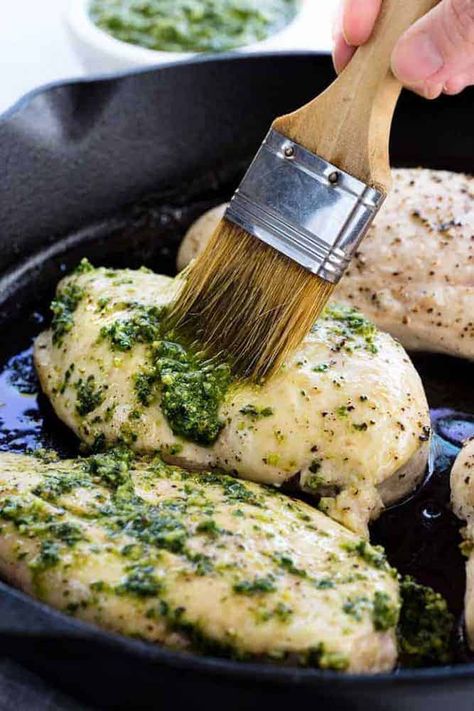 Pesto Chicken is a healthy baked dish that is loaded with flavor. The pesto sauce is made with fresh basil, spinach, garlic, walnuts and Parmesan cheese that gets added right on top of the tender chicken to make each bite irresistible! Brushing pesto sauce on chicken breasts.
