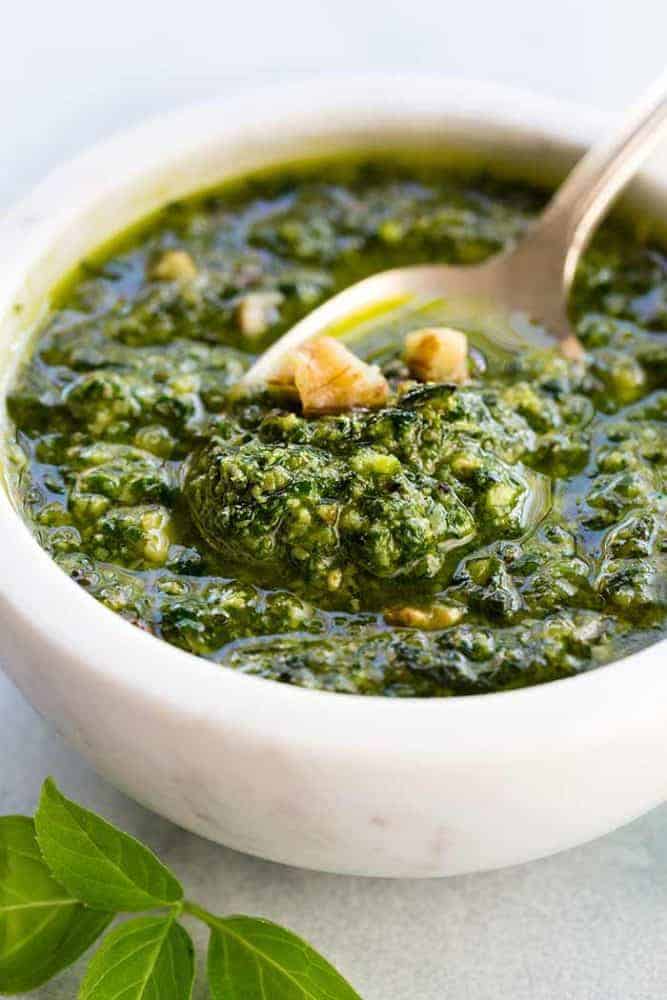 Pesto Chicken is a healthy baked dish that is loaded with flavor. The pesto sauce is made with fresh basil, spinach, garlic, walnuts and Parmesan cheese that gets added right on top of the tender chicken to make each bite irresistible! White bowl filled with homemade pesto sauce.