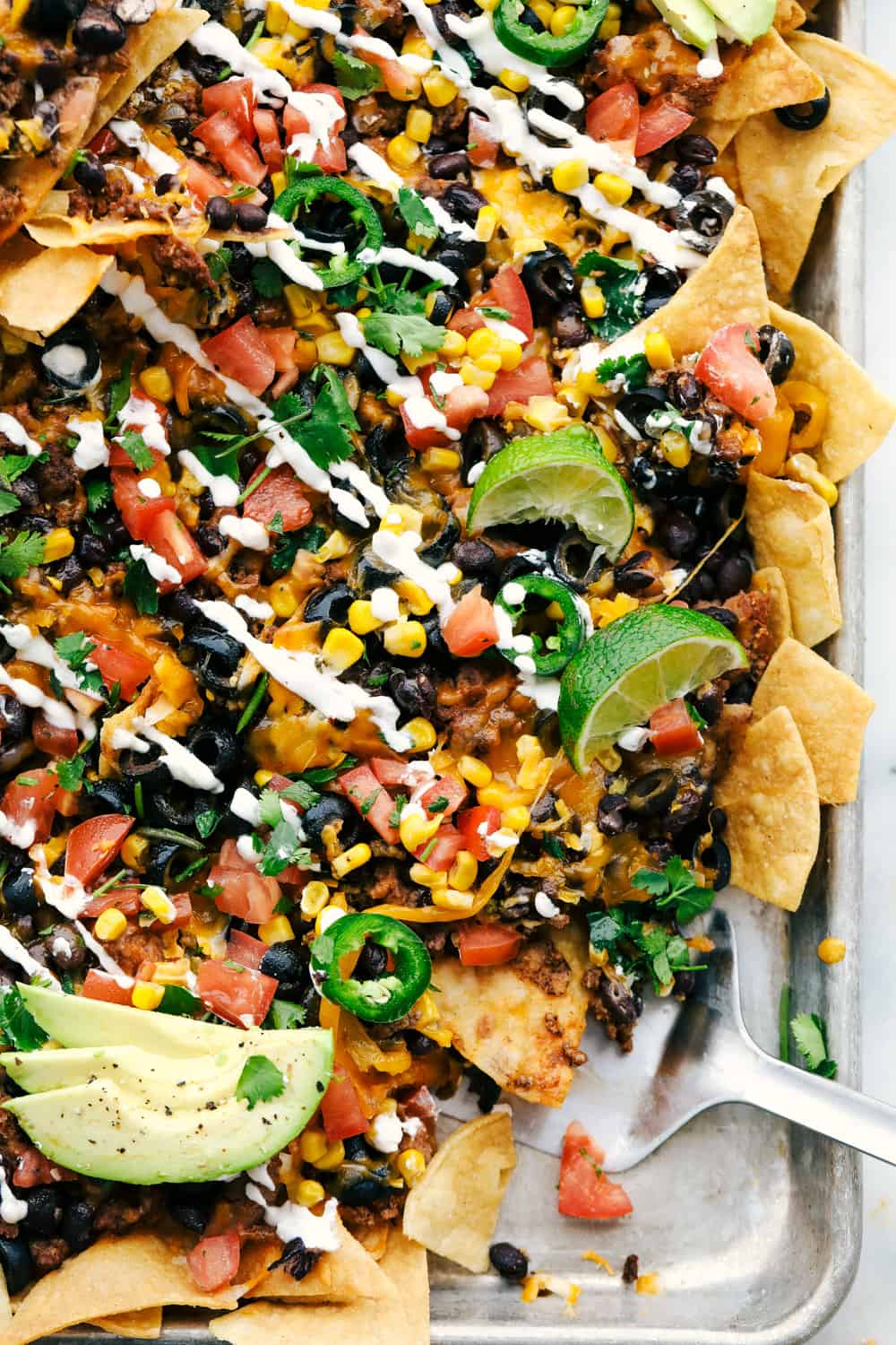 Oven Baked Sheet Pan Nachos Recipe are filled with a layer of chips, ground beef, refried beans, black olives, chopped tomatoes, corn, cheese sprinkled over top then baked to perfection! The possibilities are endless! Sheet pan nachos