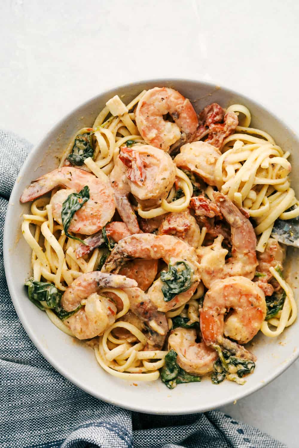 Tuscan Garlic Shrimpย is the most amazing creamy shrimp dish. A creamy garlic parmesan sauce with spinach and sun-driedย tomatoesย creates an unforgettable restaurantย qualityย meal right at home! Tuscan shrimp tossed with noodles in a bowl.
