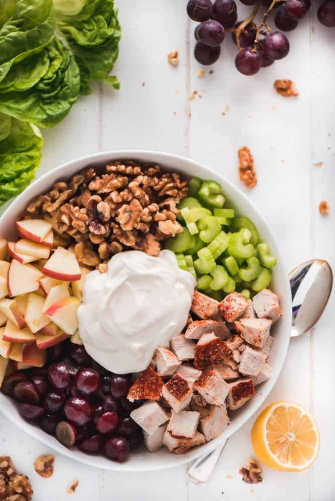 This Waldorf Chicken Salad is a refreshing and filling dish loaded with fruit, veggies, and nuts. It comes together quickly and packs up well for taking to work or even a picnic. A bowl full of Waldorf Chicken Salad ingredients- Chicken, grapes, apples, walnuts, celery, and dressing.