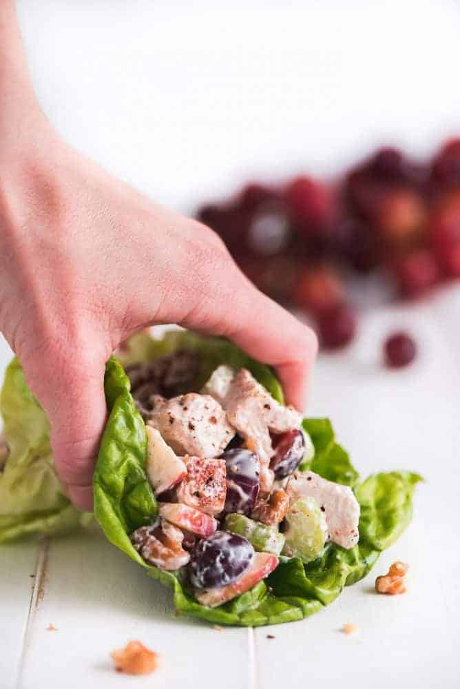 This Waldorf Chicken Salad is a refreshing and filling dish loaded with fruit, veggies, and nuts. It comes together quickly and packs up well for taking to work or even a picnic. Picking up Waldorf Chicken Salad on a bed of lettuce.
