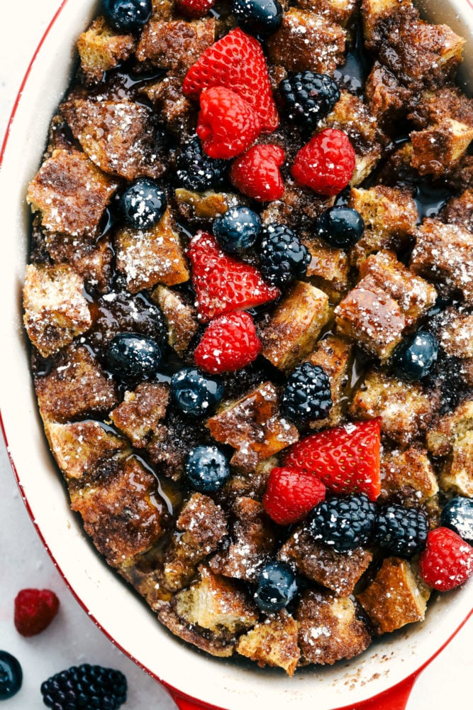 Cinnamon baked French toast is a delicious breakfast casserole full of cinnamon sugar goodness! Soft brioche bread pieces get baked in a sweet creamy custard. French toast has never been easier! Baked French toast in a pan with fresh raspberries, strawberries and blueberries over top.