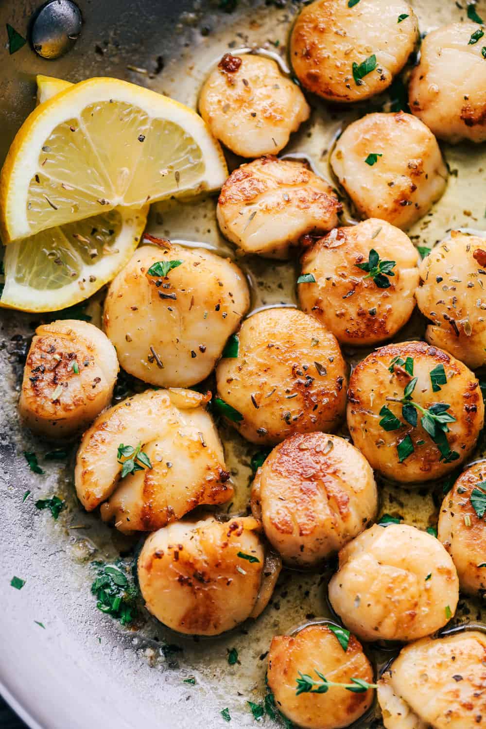 Garlic Butter Herb Scallops are pan seared and have the best buttery garlic herb sauce. This is a quick and simple meal that tastes straight from a restaurant!ย Scallops cooking in pan.