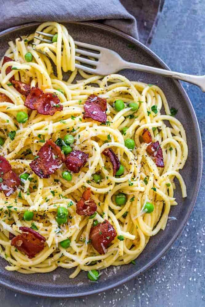 Pasta Carbonara is a favorite Italian dish made with wholesome ingredients. The creamy sauce is made with eggs and Parmesan cheese, using a special technique to ensure a smooth and luscious texture. Spaghetti noodles are topped with chopped bacon and sweet peas for the ultimate comfort food. Plate of pasta carbonara with a fork.