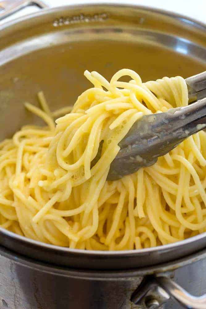 Pasta Carbonara is a favorite Italian dish made with wholesome ingredients. The creamy sauce is made with eggs and Parmesan cheese, using a special technique to ensure a smooth and luscious texture. Spaghetti noodles are topped with chopped bacon and sweet peas for the ultimate comfort food. Metal tongs picking spaghetti noodles out of a metal bowl.