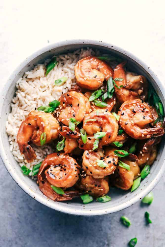Sticky Sesame Garlic Shrimp is coated in the most amazing sticky Asian sauce and topped with green onions and sesame seeds! This is a quick and easy 30-minute meal that you will make again and again! Sticky Sesame Garlic Shrimp over white rice in a white bowl.